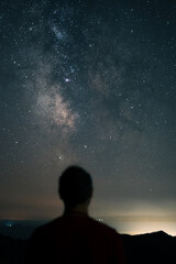 The Milky Way in the night sky and a blurred silhouette of a person standing and looking at it