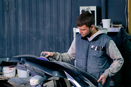 auto mechanic at a service station polishing the front part of dark blue car