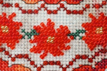 A close-up shot of a cross stitched ornament with red beads flowers made with white and red threads.