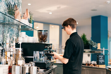 Young barista making coffee at automatic machine in a modern coffee shop. Student working part-time in cafe. Problems of unemployment and Job opportunities for youth. Small business vacancies - Powered by Adobe