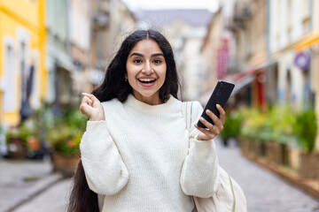 Portrait of a happy and excited young Indian girl in a white sweater standing in the middle of a...