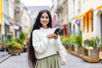 Portrait of a happy Indian girl standing in the middle of a city street and holding a mobile phone....