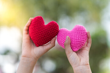 Man hand holding a red heart and pink heart with love in sunlight in the public park, For...
