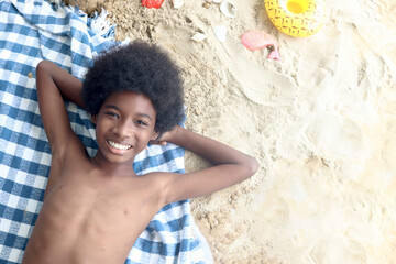 Portrait of An African boy with curly hair on the beach. Top view of happy smiling kid lying on...