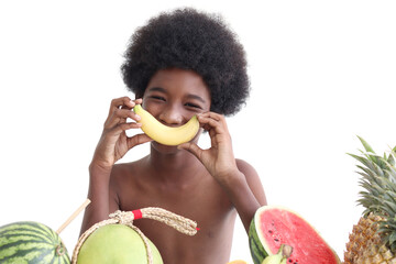 Portrait of African boy with curly hair sitting behind the row of tropical fruits. Happy smiling...