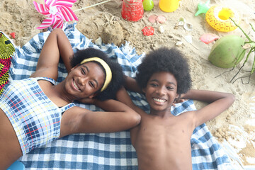 Portrait of African curly hair boy and girl sibling on the beach. Top view of happy smiling kid friend lying on sand beach and looking at camera. Joyful children resting on holiday at the sea.