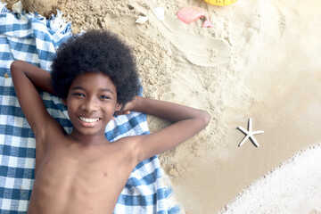 Portrait of An African boy with curly hair on the beach. Top view of happy smiling kid lying on...