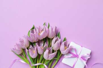 Womens day or mothers day greeting card. Gift box and heap of fresh beautiful tulip flowers on pastel lilac table top view.