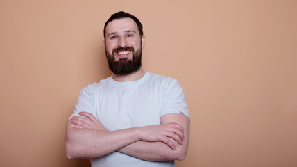 man with a beard is smiling and wearing a white shirt. He is standing in front of a tan wall