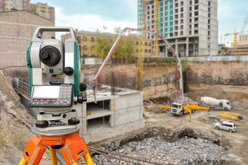 Surveyor equipment at construction site. Geodetic device on tripod. Optical theodolite near house under construction. Electronic surveyor tool. Equipment for measuring work in geodesy - obrazy, fototapety, plakaty