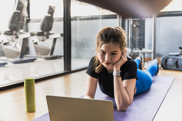 Sportswoman looking at laptop computer and doing exercise in fitness gym