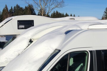 Schneebedeckte Wohnmobile auf einem Parkplatz. Camping im Winter. Allgäu, Bayern.