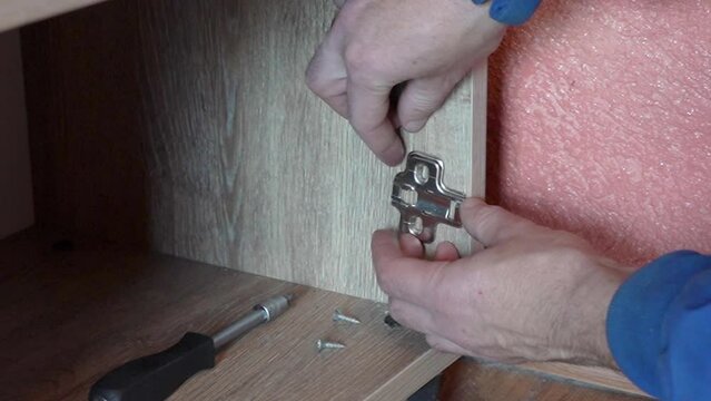 a man installs hinges in furniture, a man puts a metal bar to install hinges in furniture, furniture repair