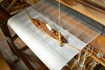 Weaving shuttle, spndle and yarn on loom. Warp and weft of white fabric