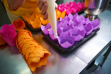 Qualified pastry cook is filling disposable cake molds with dough