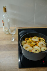 On the induction stove there is a gray pan with white wine and slices of apples, oranges and spices...