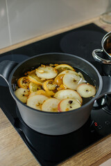 There is a gray pan with white wine and slices of apples, oranges and spices for mulled wine on the...