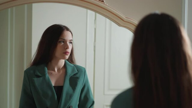 Pensive woman stands by mirror. Brunette lady has issues with self esteem evaluating looks in reflection at home. Mental state disorder symptoms