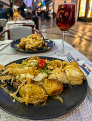 codfish with potatos on a plate in a restaurant in Rua Augusta street, glass of sangria in the background