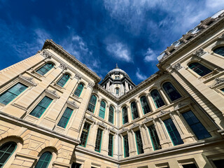 Fototapeta premium Rear views of the Illinois State Capitol Building in Springfield, Illinois, USA. Cloudy blue skies overhead. The US flag, State of Illinois Flag, and Black History Month Flag fly atop the dome.