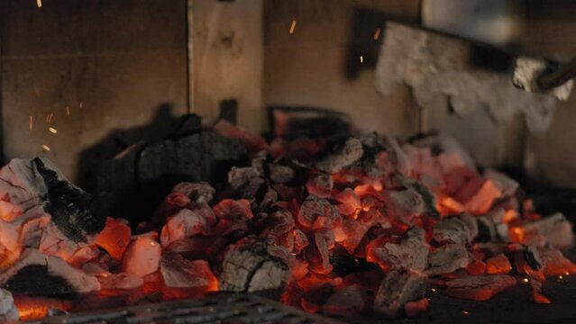 Black chef rakes coals into a wood-fired grill in slow motion