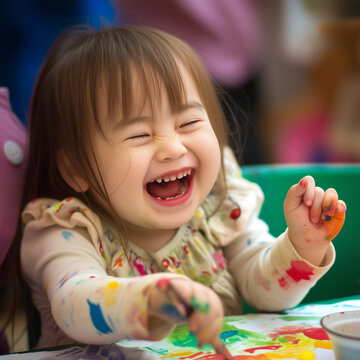 Happy girl artist with Down syndrome paints with paint on her hands