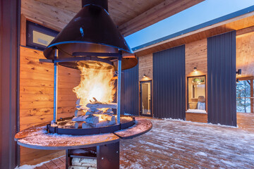 A snow-covered terrace with a lighted barbecue grill on a winter evening. Wooden house-chalet for...
