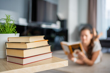 Stack of books in the foreground and woman reads a book lying down in the background