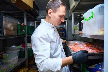 Kitchen employee with a tray in a restaurant refrigerator