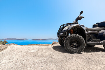 Quad bike parked on the seafront of the Akrotiri peninsula in the southwestern part of the island of Santorini with a view of the volcanic caldera of Nea Kameni.  - obrazy, fototapety, plakaty