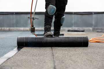 professional roofer applying bitumen roll on flat roof with a gas burner at a modern construction...