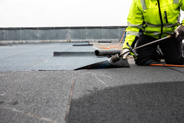 professional roofer applying bitumen roll on flat roof with a gas burner at a modern construction...