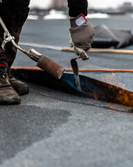 professional roofer applying bitumen roll on flat roof with a gas burner at a modern construction site - obrazy, fototapety, plakaty