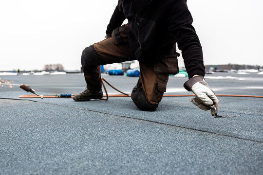 professional roofer applying bitumen roll on flat roof with a gas burner at a modern construction site