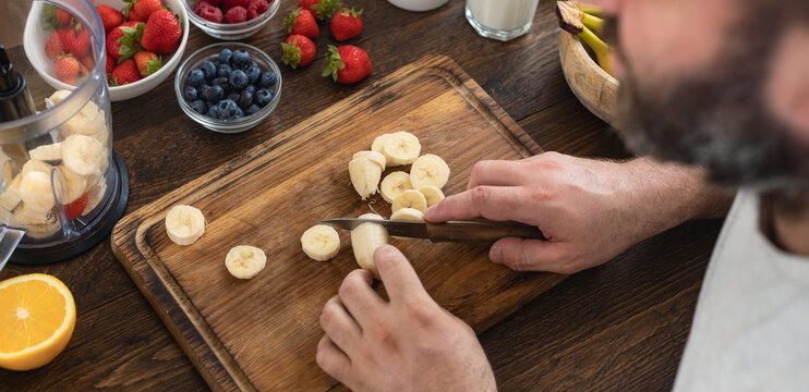 A man prepares a nutritious banana-strawberry smoothie in his home kitchen. Healthy lifestyle concept