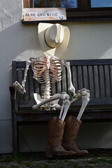 Park and Ride. Skelett mit Cowboyhut sitzt auf einer Holzbank