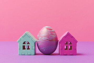 Decorative easter egg painted in fluid art technique and houses against pink background with copy space