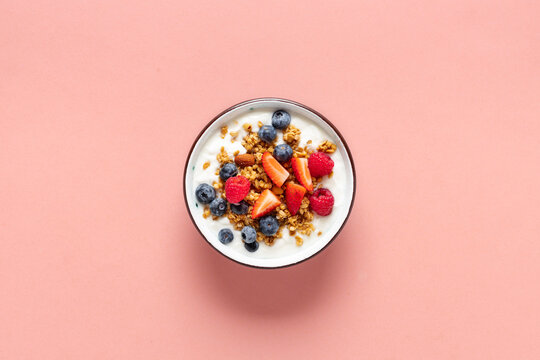Healthy breakfast bowl with ingredients granola fruits Greek yogurt and berries on a pink background top view. Weight loss, healthy lifestyle and eating concept