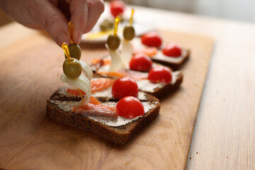 Olives and onions are added to the sandwich. Preparation of canapes with fish and vegetables
