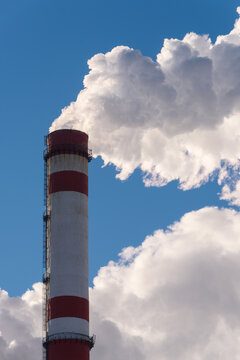 Industrial pollution of the environment. Plumes of white smoke from a chimney against a blue sky background, vertical frame.