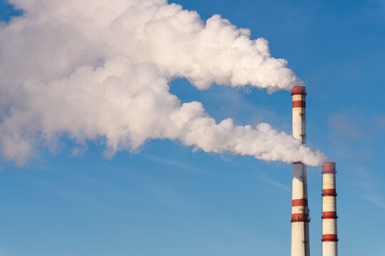 Industrial pollution of the environment. Plumes of white smoke from a chimney against a blue sky.