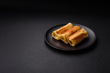 Delicious fried pancakes with filling rolled on a dark concrete background