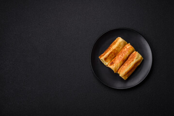 Delicious fried pancakes with filling rolled on a dark concrete background