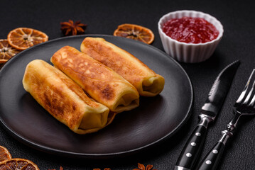 Delicious fried pancakes with filling rolled on a dark concrete background