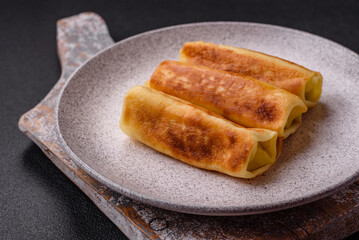 Delicious fried pancakes with filling rolled on a dark concrete background