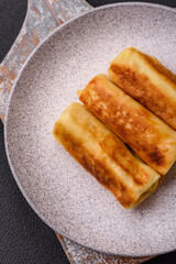 Delicious fried pancakes with filling rolled on a dark concrete background