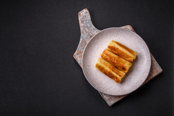 Delicious fried pancakes with filling rolled on a dark concrete background