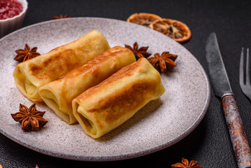Delicious fried pancakes with filling rolled on a dark concrete background