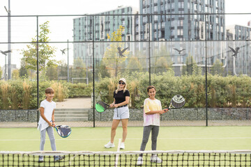 Obraz premium Young sporty woman with children playing padel game in court on sunny day