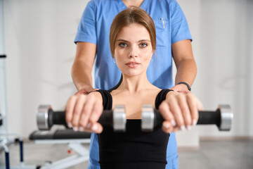 Patient performs exercises with dumbbells under supervision of physiotherapist
